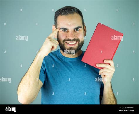 Young man pointing his head while holding a red book Looking at camera ...