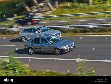 Two cars speeding along a motorway, one overtaking the other. Motion blur used to give a sense ...