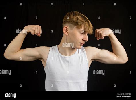 Portrait of a 14 year old caucasian teenage boy wearing a sleeveless vest flexing both his ...