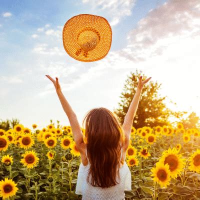 a woman standing in a sunflower field with her arms raised up to the sky