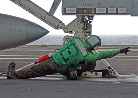 A Navy flight deck crewman brings an aircraft into launch position.