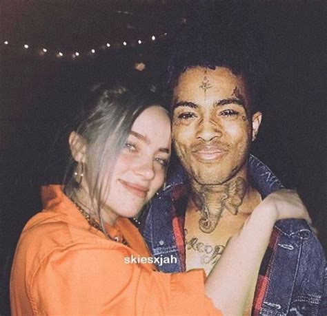 a woman hugging a man with tattoos on his face and chest in an orange shirt