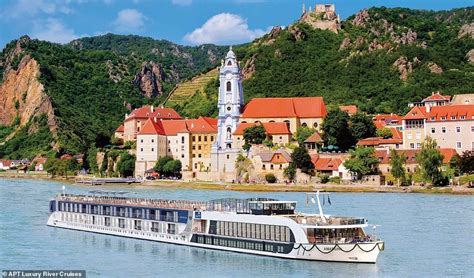 a river cruise boat on the water in front of a town with mountains ...