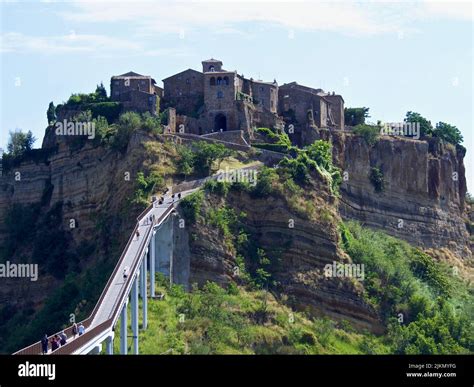 A steel bridge with people walking to the Civita di Bagnoregio village on the hill Stock Photo ...