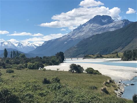 a river running through a lush green valley next to a mountain covered with snow capped mountains