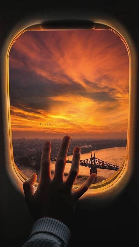 someone is holding their hand out the window of an airplane as the sun goes down