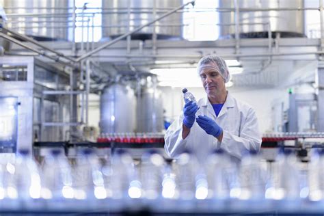 Worker inspecting water bottle on production line in spring water factory - Stock Photo - Dissolve