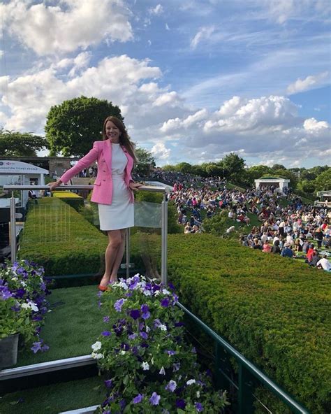 a woman in a pink jacket and white dress standing on a balcony with purple flowers