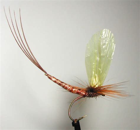 an orange and yellow fly on a black hook with long brown hair, sitting on a white surface