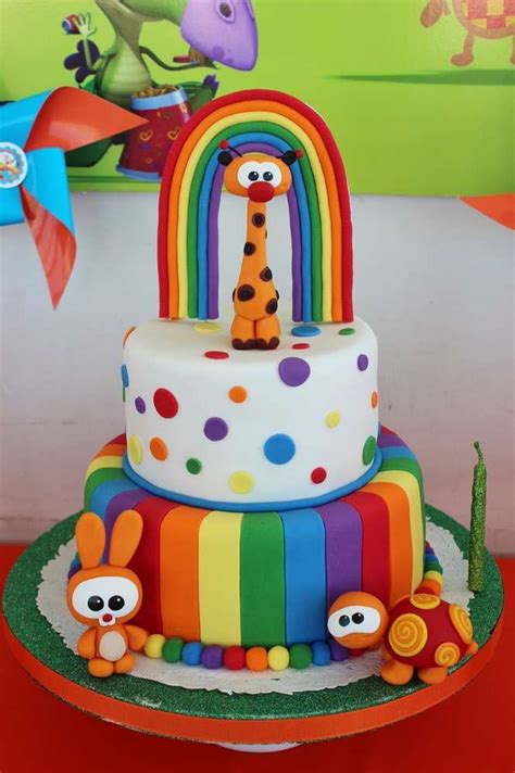 a multi - tiered cake decorated with colorful fondant and cartoon characters is displayed on a table