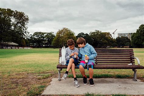 "Two Boys Sitting On Bench In Park Sharing Food" by Stocksy Contributor "Trent Lanz" - Stocksy