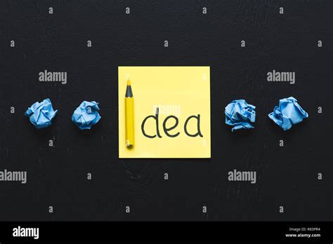 'idea' word written on sticky note and blue crumpled paper balls on black background, ideas ...