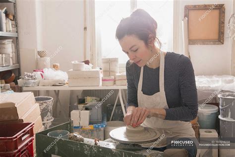 Caucasian woman is shaping pottery clay on a pottery wheel in a ceramic workshop. — interior ...