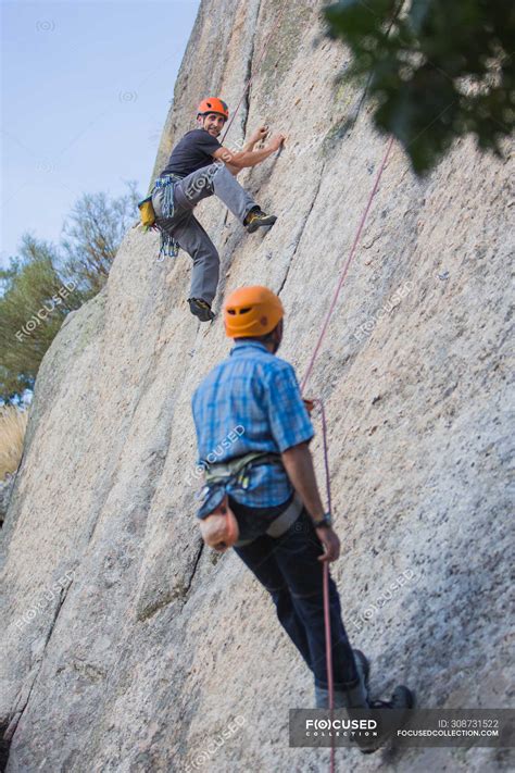 Adventurers climbing mountain wearing safety harness against ...