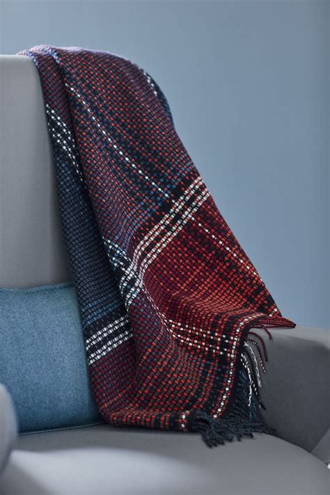 a blue and red plaid blanket sitting on top of a gray couch next to a ...