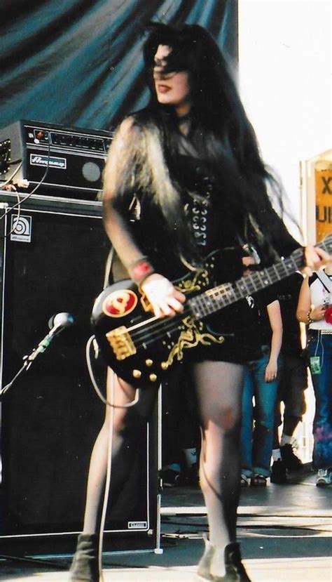 a woman with long black hair is holding a guitar and standing in front ...