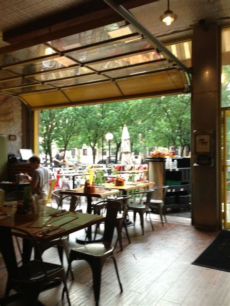 the inside of a restaurant with tables, chairs and an open glass door that leads to a patio