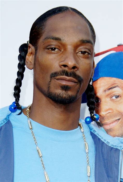 a man with braids and a blue shirt is posing for the camera in front of a poster