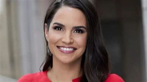 a woman with long dark hair wearing a red top and smiling at the camera while standing in front ...