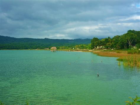 a body of water with trees in the background and clouds in the sky above it