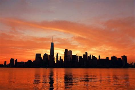 an orange and pink sky is reflected in the water as the sun sets over new york city