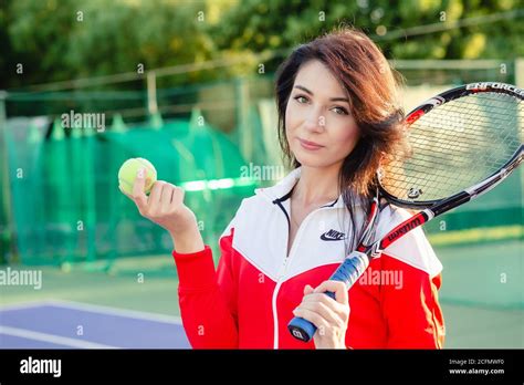 Portrait of a beautiful young female tennis player in sports clothing holding tennis racket on ...