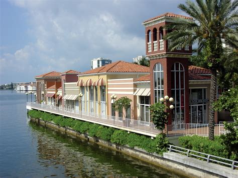 a row of houses on the side of a body of water with palm trees and buildings in the background