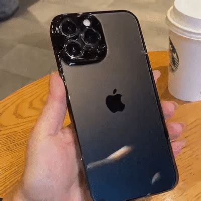 a person holding an iphone in their hand at a table with a cup of coffee