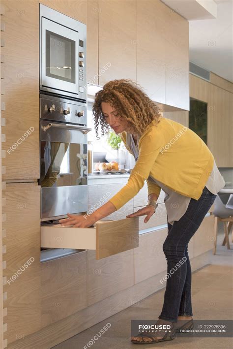 Woman in casual outfit opening drawer in kitchen — brown hair, Mid Adult - Stock Photo | #222925806