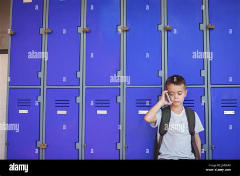 Boy talking on mobile phone while standing against lockers at school Stock Photo - Alamy
