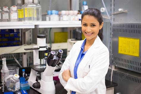 Closeup portrait, young smiling scientist in white lab coat standing by microscope. Isolated lab ...