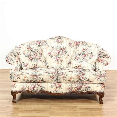 This cottage chic loveseat is upholstered in an off white cream fabric with a light floral ...