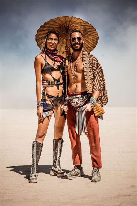 two people standing in the desert with an umbrella over their heads and ...