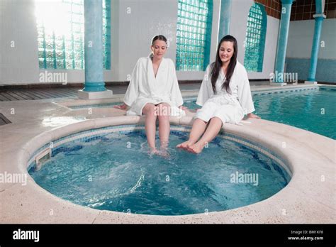 Two women sitting at the poolside with their feet soaking in water ...