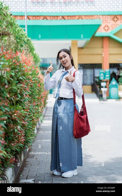 full body shot of a smiling student wearing an Indonesian high school uniform with a thumbs up ...