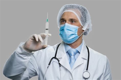 Premium Photo | Male doctor preparing syringe for injection. Doctor in face mask and hat holding ...