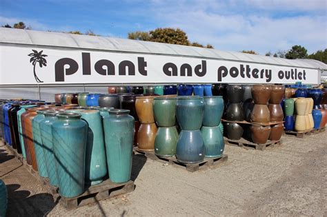 there are many vases that are on the ground in front of a sign for plant and pottery outlet