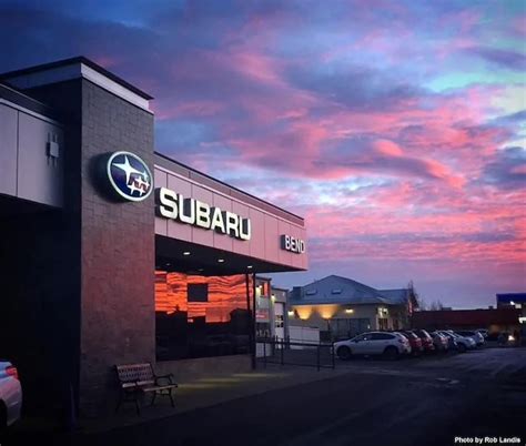 a subaru car dealership at dusk with the sun setting in the sky behind it