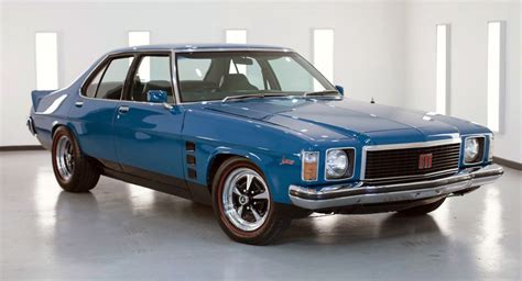 an old blue car is parked in a room with white walls and windows on the wall