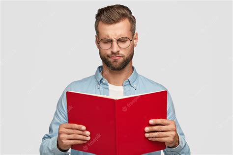 Free Photo | Serious clever young male teacher with trendy haircut, carries red book, loos hesitant