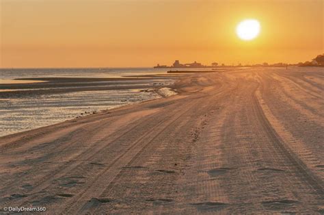 the sun is setting over the beach with footprints in the sand