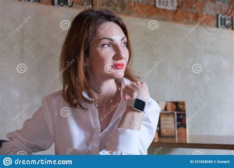Portrait of an Attractive Young Woman with Red Hair in White Shirt at a Wooden Table in a Cafe ...