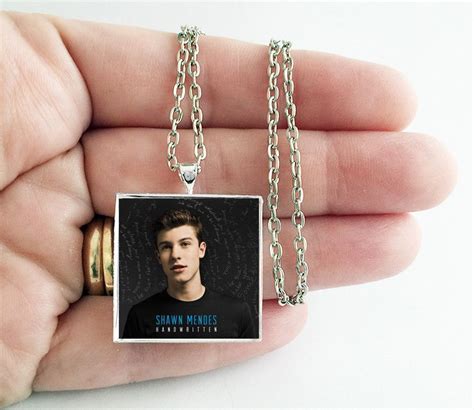 This is a necklace featuring album art of the "Handwritten" record by Shawn Mendes sealed in a ...