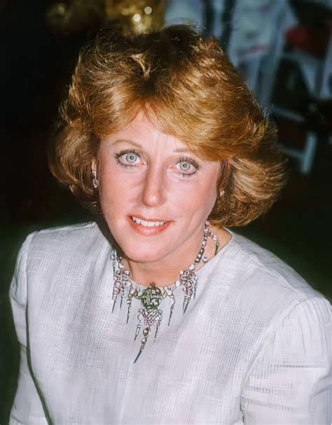 a woman with blonde hair wearing a white shirt and necklace sitting in ...