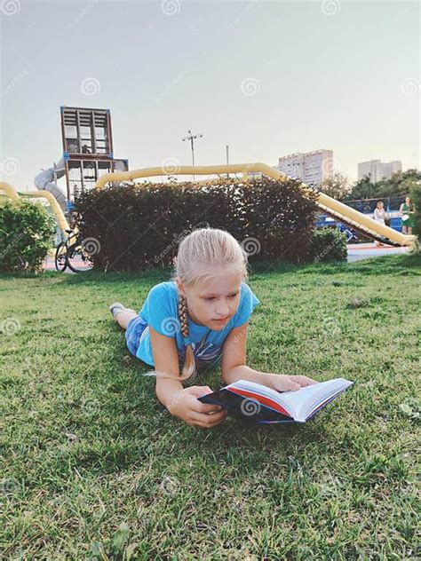 A Little Girl is Lying on the Grass and Reading a Book. Childhood Stock ...