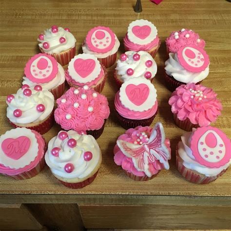 cupcakes decorated with pink and white icing on a wooden counter top,