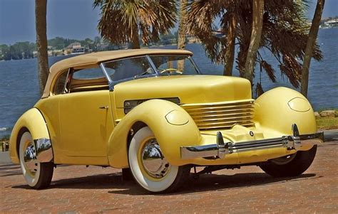 an old yellow car parked in front of some palm trees and the water behind it