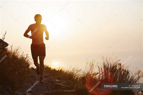 Silhouette of man running on trail with sunset ocean in background ...