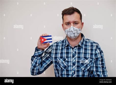 Man in checkered shirt show Cuba flag card in hand, wear protect mask ...