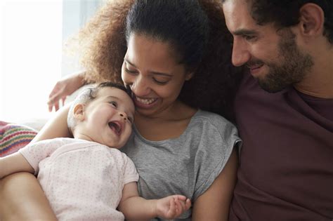 Parents Sitting On Sofa Cuddling Baby Daughter At Home - New Life ...